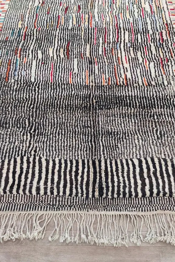 Multicolored Moroccan woven rug with fringe on a wooden floor