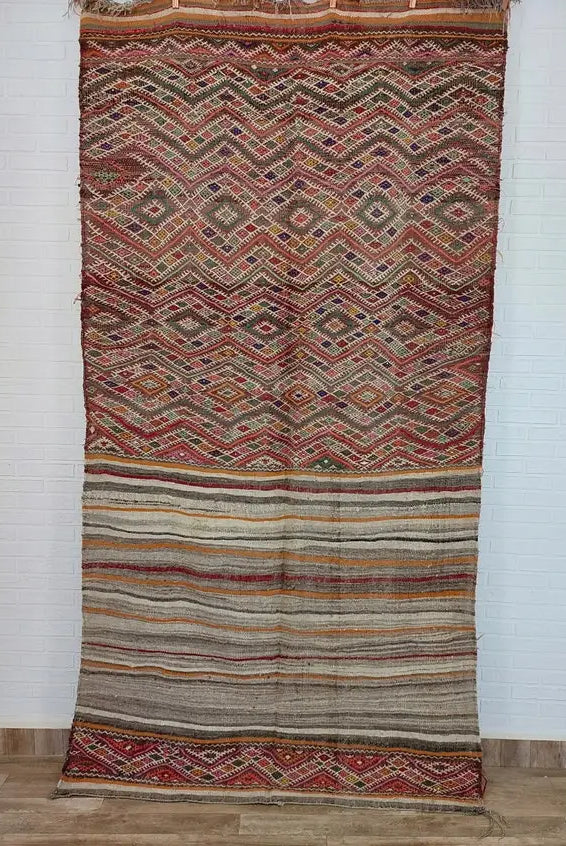 Traditional patterned Moroccan rug on a wooden floor with a vase and decorative elements.
