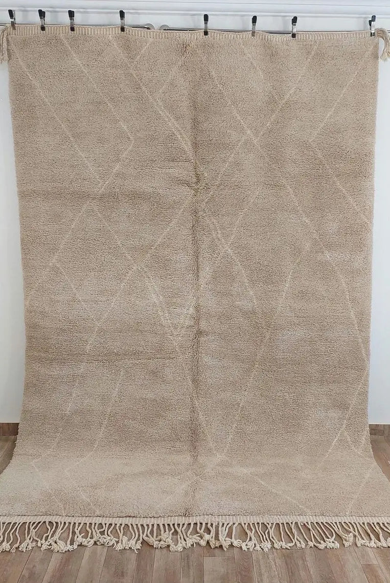Moroccan beni mrirt Beige woven rug with geometric pattern on a wooden floor against a white wall.