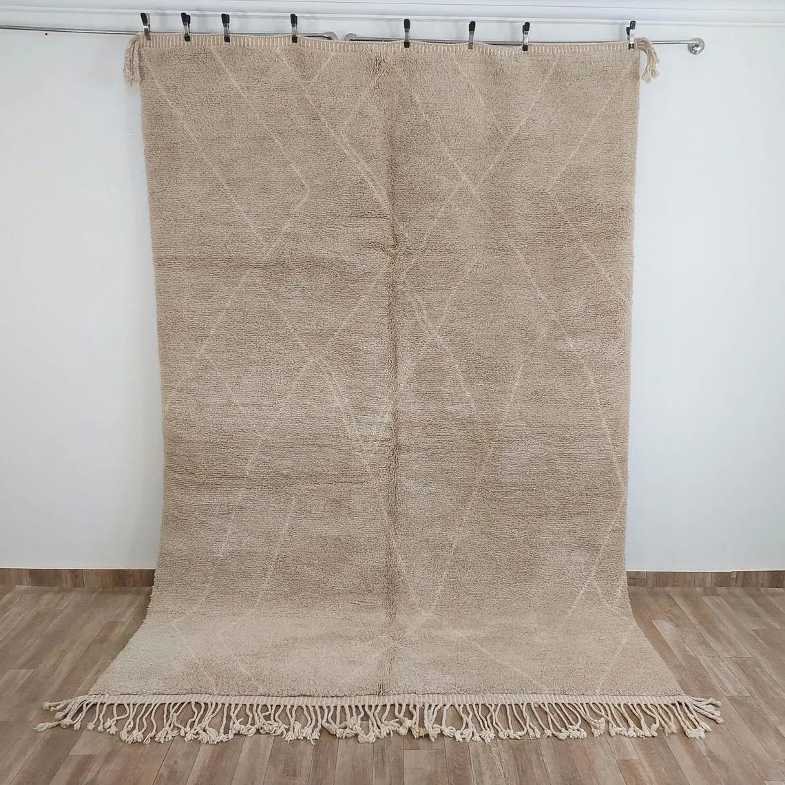 Moroccan beni mrirt Beige woven rug with geometric pattern on a wooden floor against a white wall.