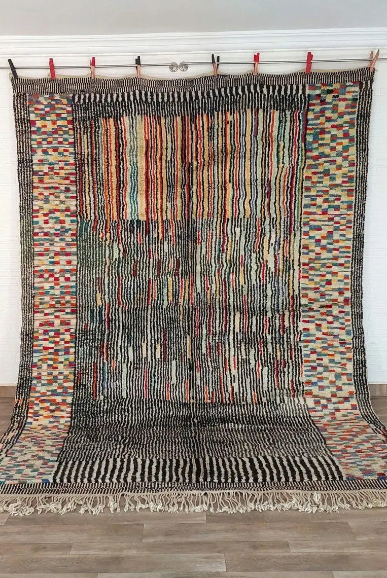 Multicolored handwoven beni mrirt rug with geometric patterns hanging on a rod against a white wall.