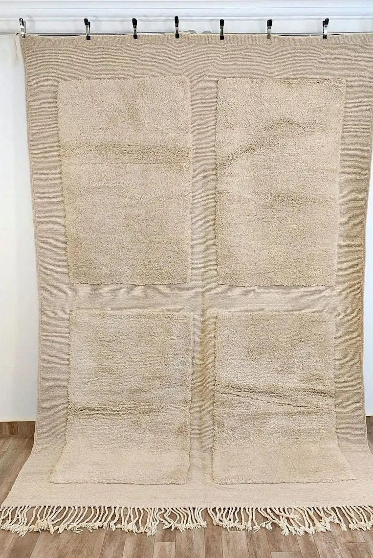 Beni mrirt Beige woven rug with four square patterns and fringe on a wooden floor.