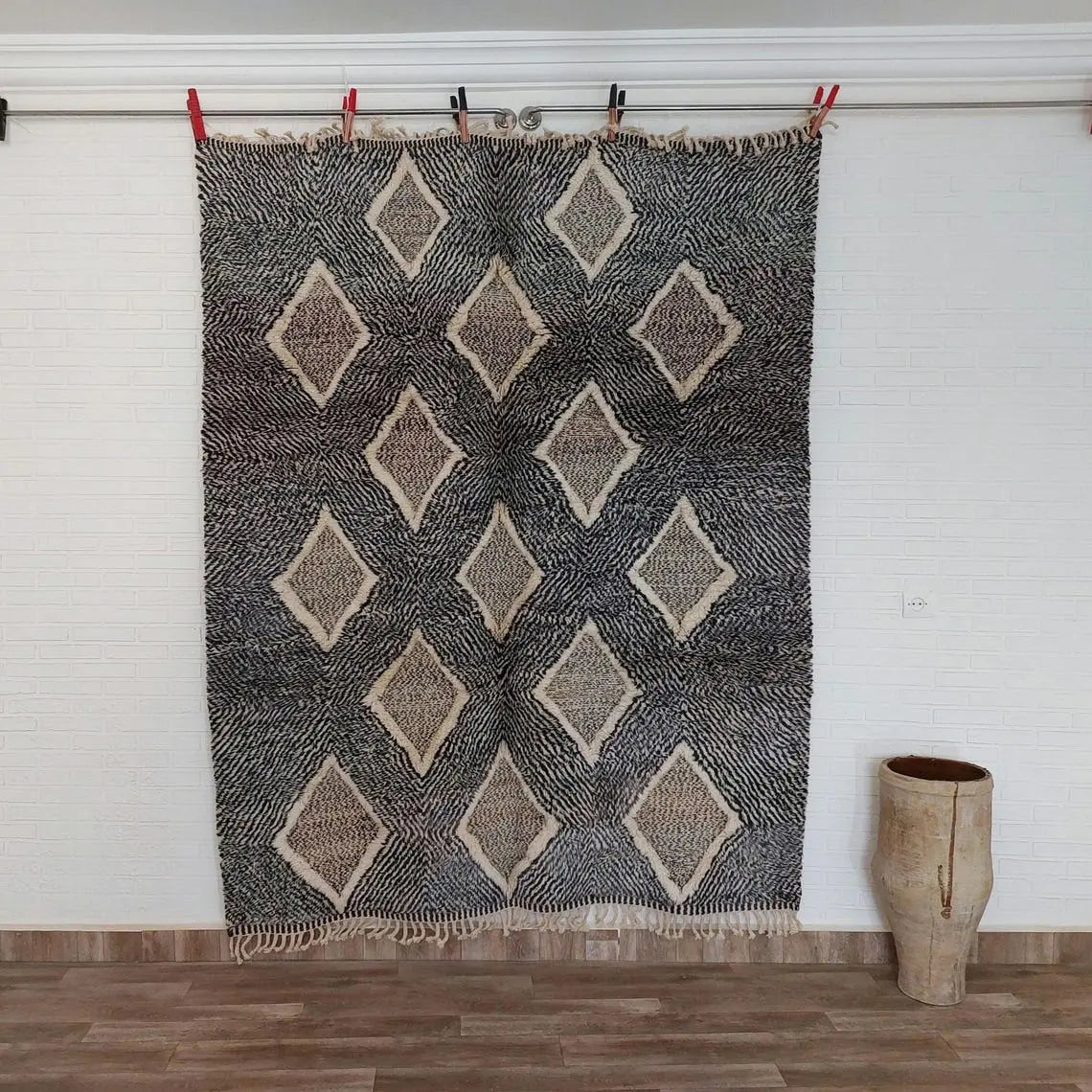 Moroccan rug with geometric pattern hanging on a line against a white wall.