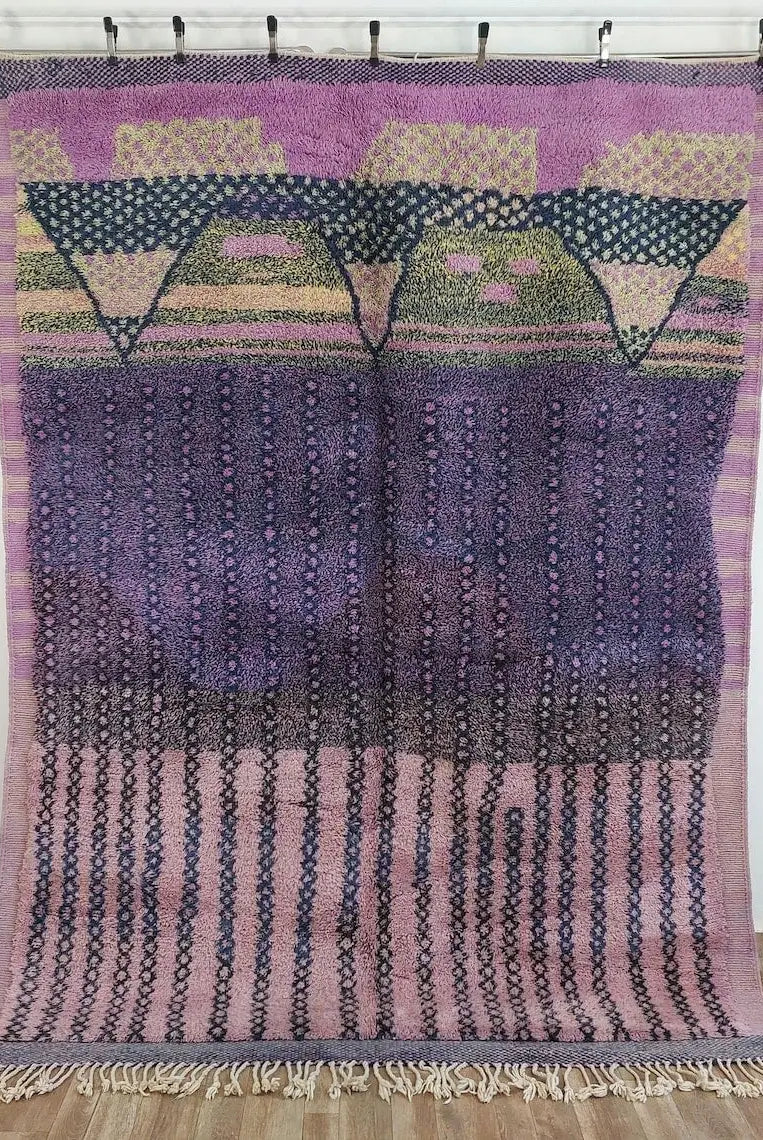 Moroccan beni mrirt rug handWoven textile with geometric patterns in purple, pink, and green on a wooden floor.