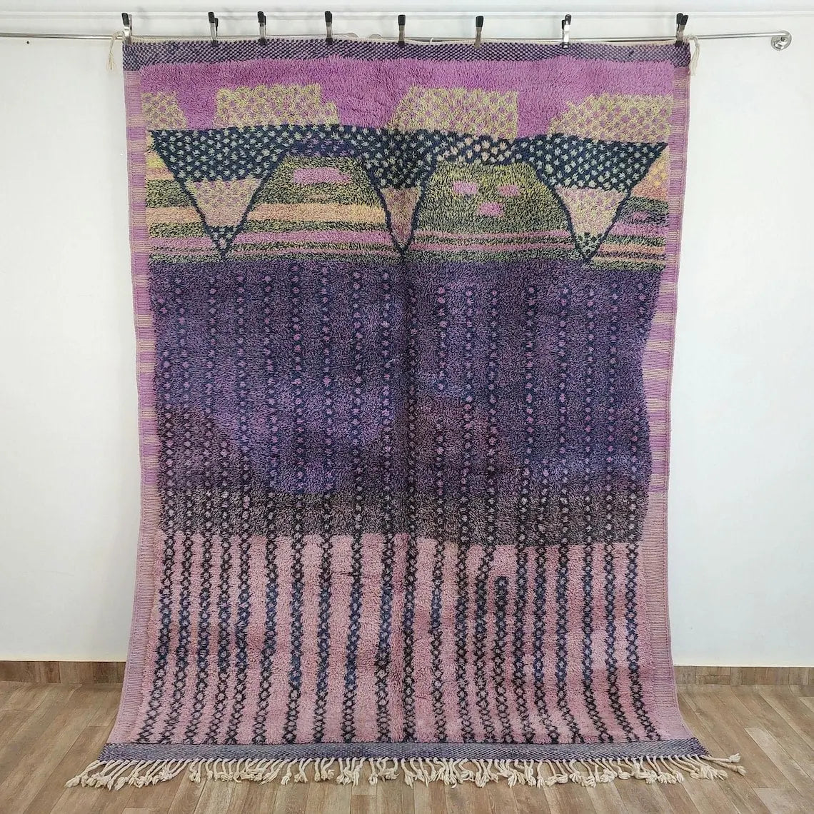 Moroccan beni mrirt rug handWoven textile with geometric patterns in purple, pink, and green on a wooden floor.