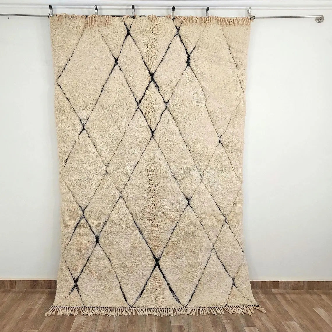 Beni mrirt Beige and black diamond patterned rug on a wooden floor with white walls.