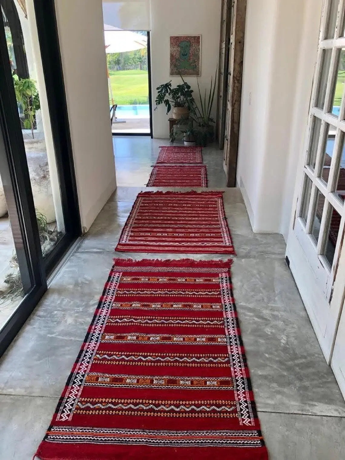 Red patterned rugs on a concrete floor with a glass door and outdoor view in the background.