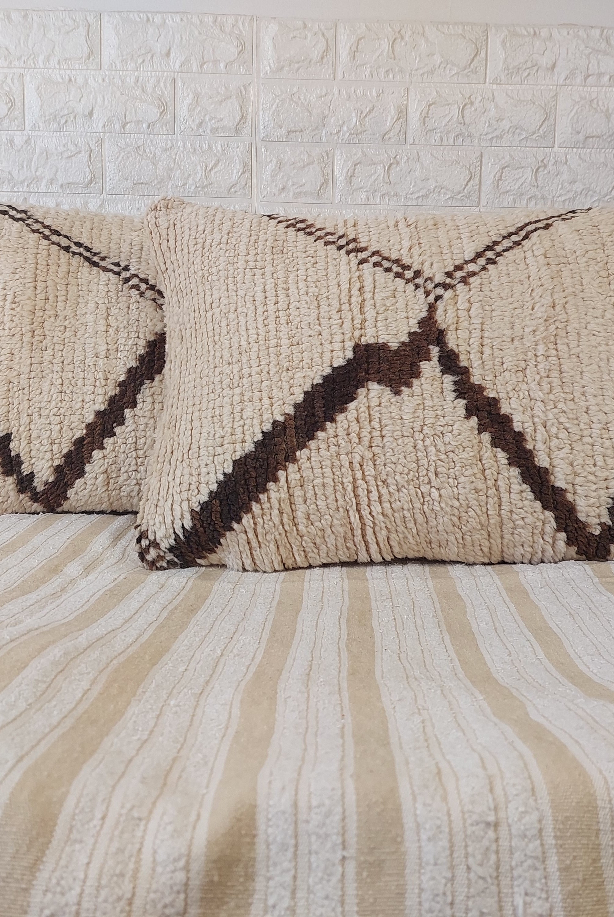 Two patterned pillows on a bed with a textured wall background