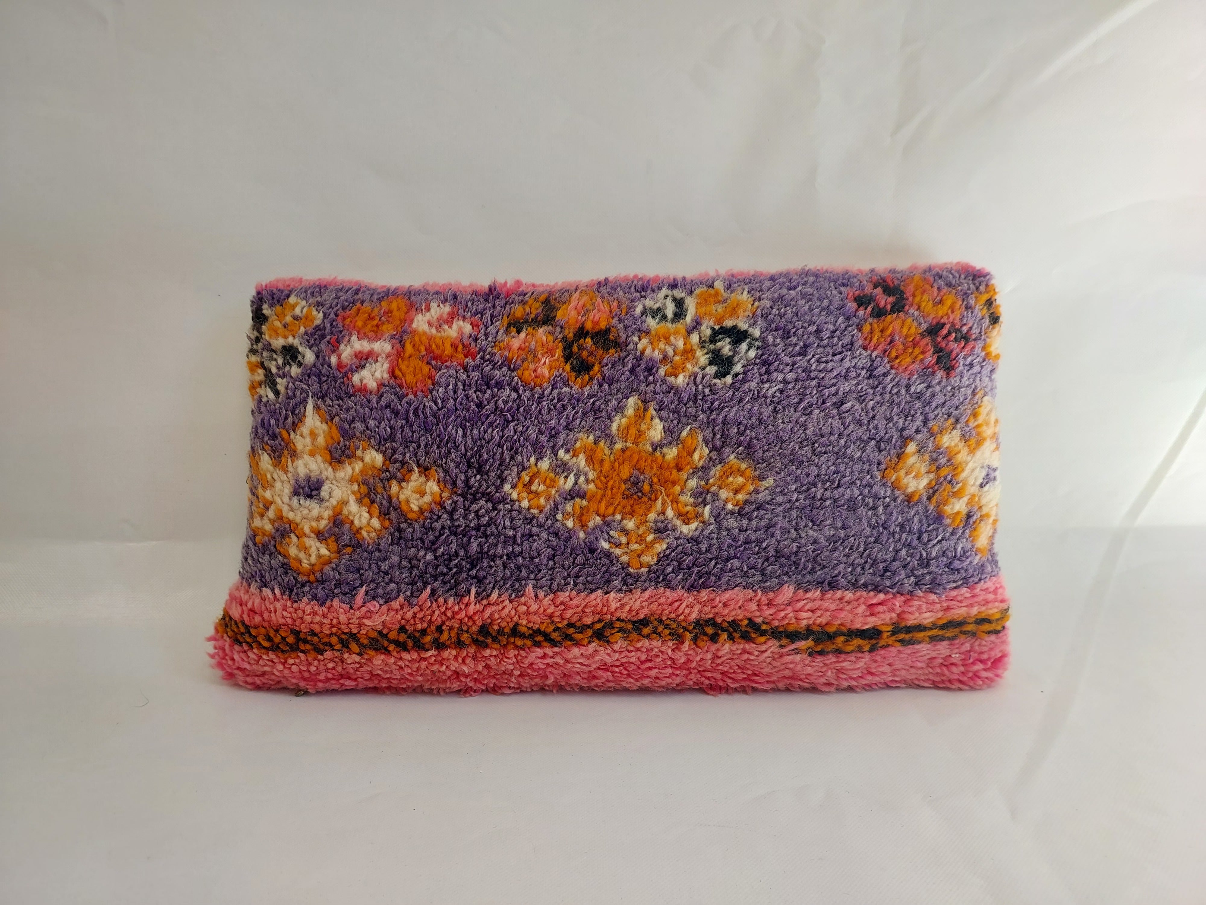 Front view of a handmade Moroccan lumbar pillow cover made from a vintage wool rug, featuring a textured purple background, orange and white geometric Amazigh motifs, and a bright pink border.