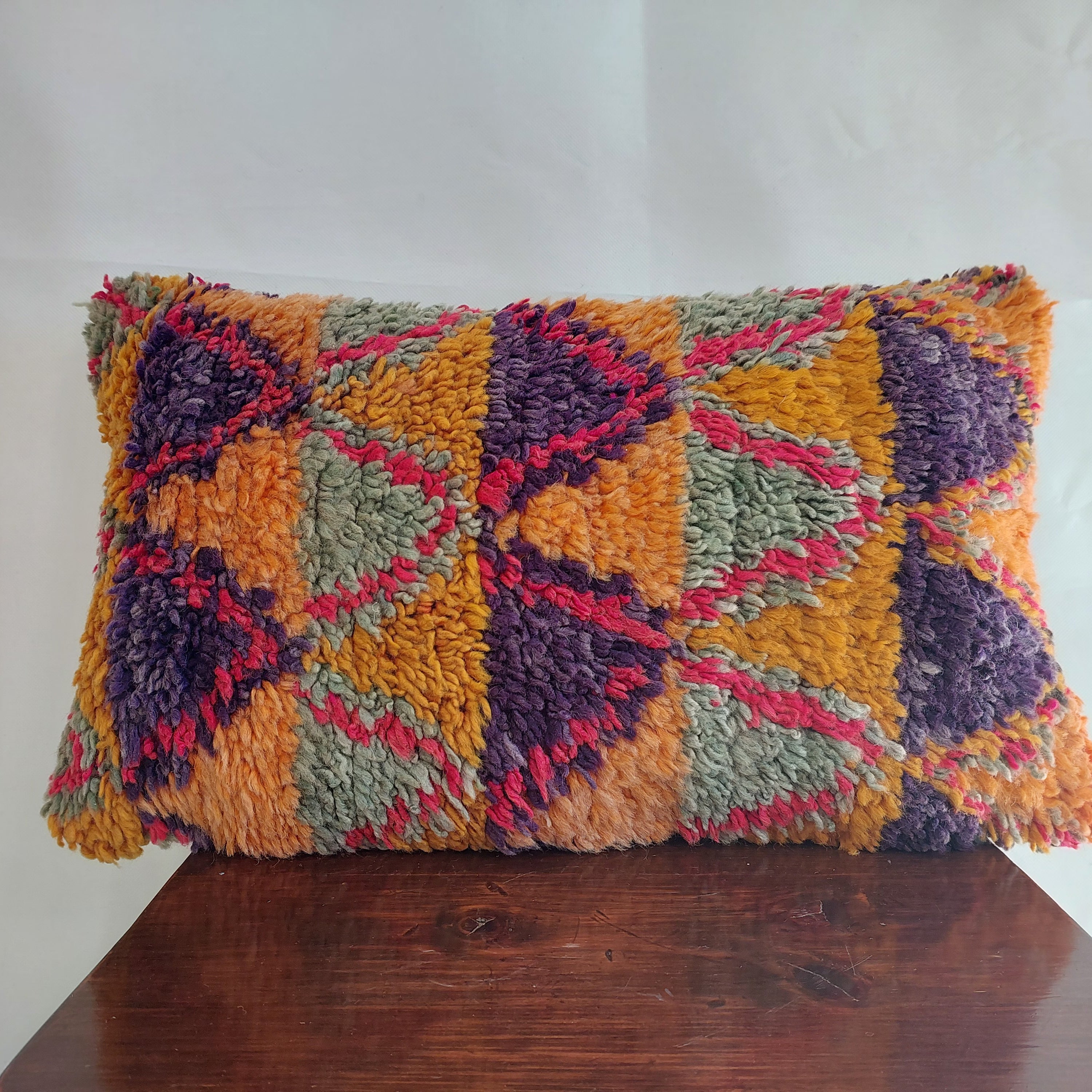Colorful textured pillow on a wooden surface with a white background