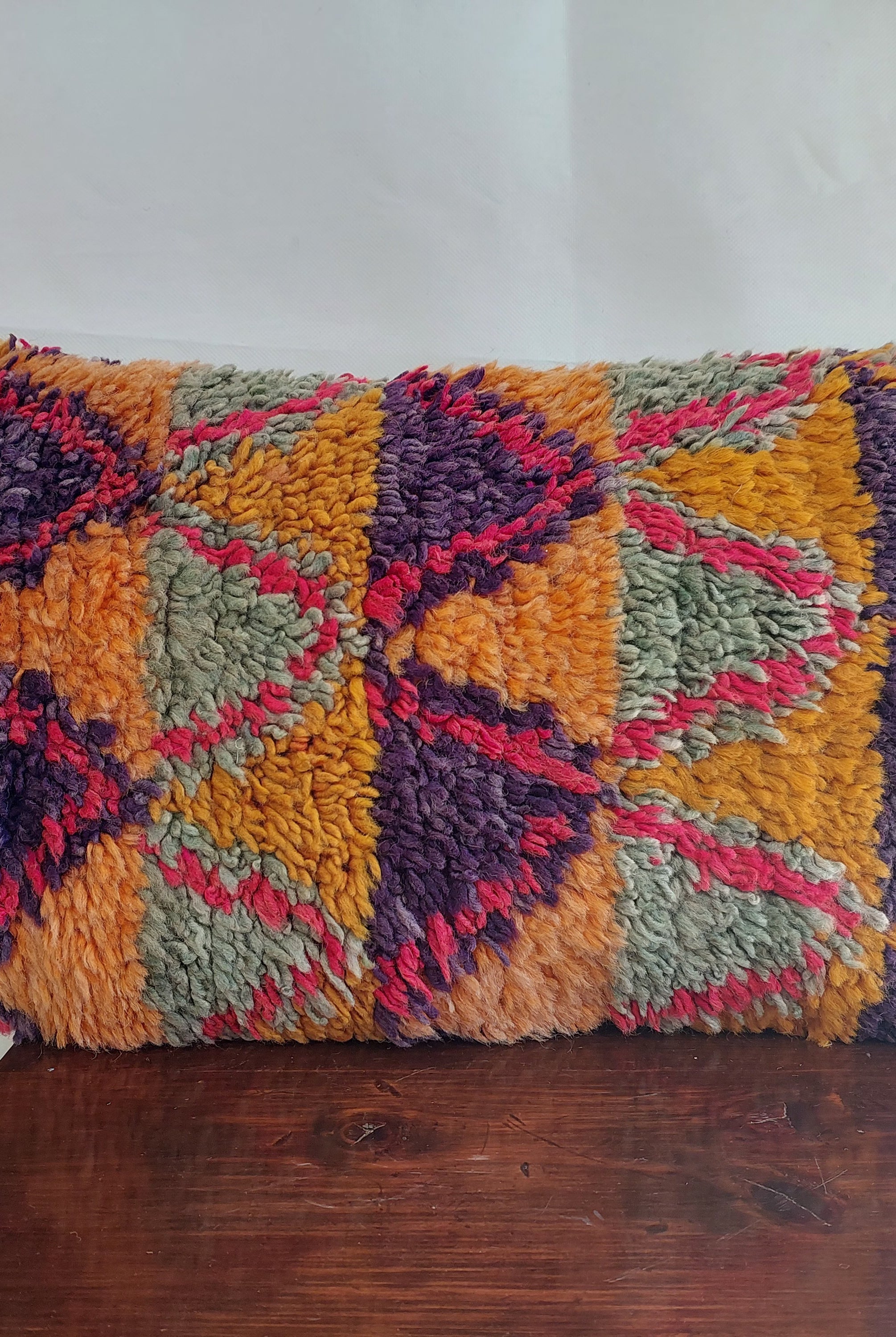 Colorful textured pillow on a wooden surface with a white background