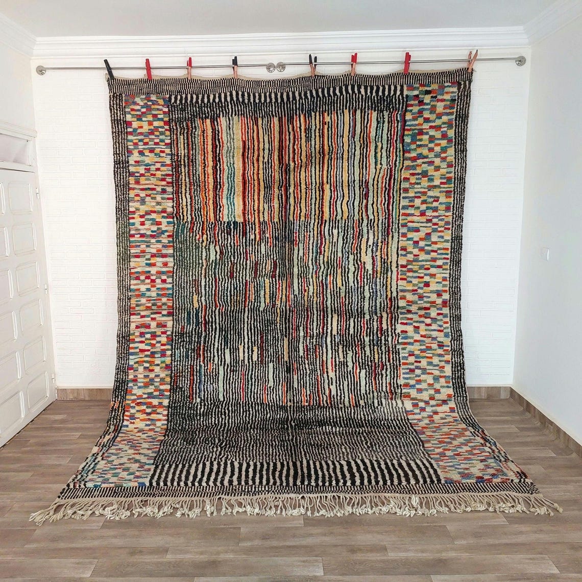 Multicolored handwoven beni mrirt rug with geometric patterns hanging on a rod against a white wall.