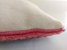 Close-up side view of a Moroccan throw pillow showing the thick, plush pink and purple wool pile of the front rug meeting the plain, cream-colored woven wool blanket fabric on the back.