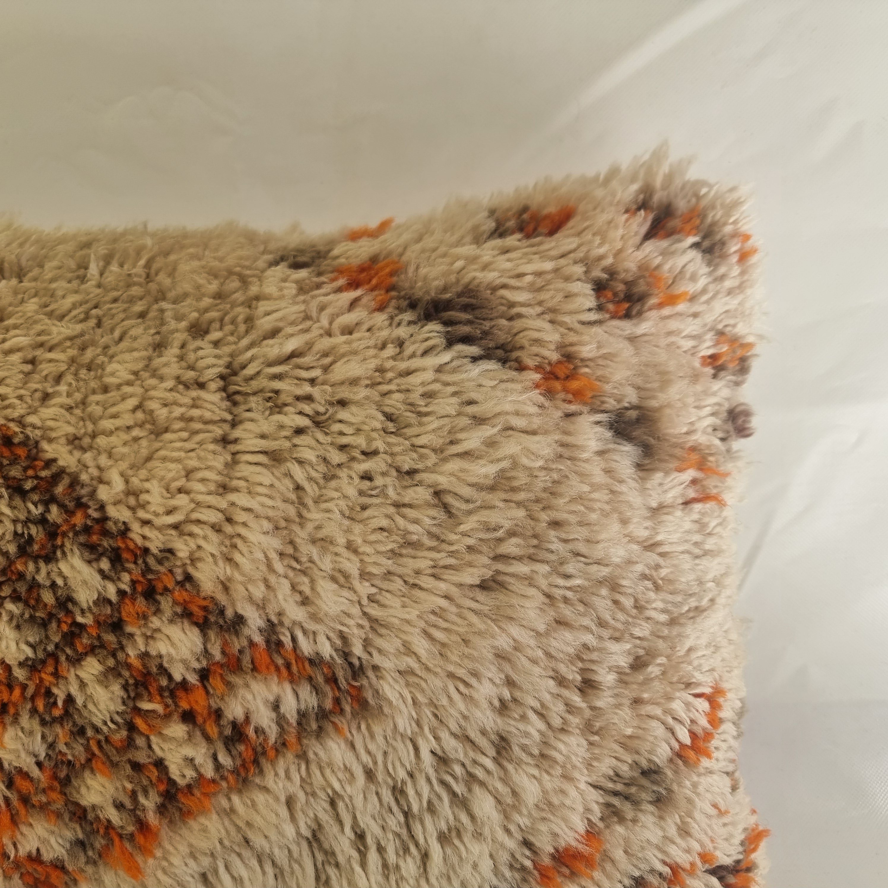 Textured beige and orange beni pillow on a white floor